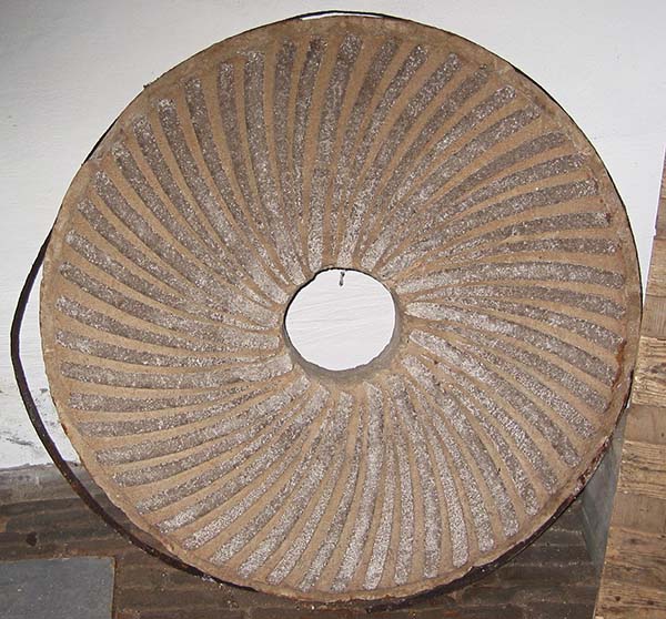 A large red-brown composite millstone with a sickle-type dressing pattern, manufactured from artificial stone in the Netherlands.